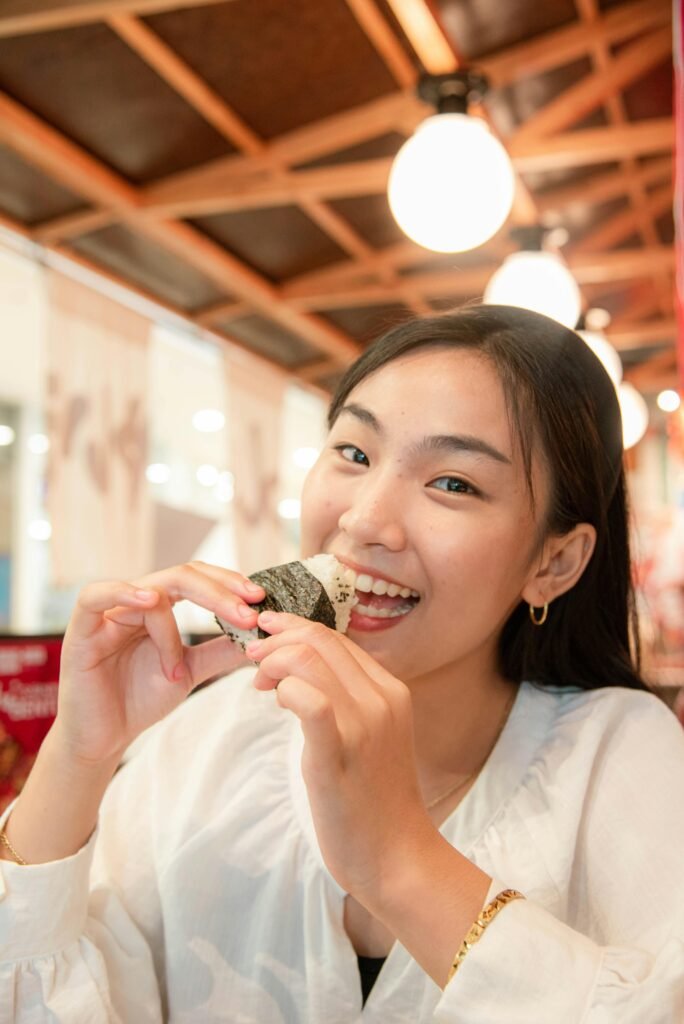 Smiling Asian woman eating onigiri in a cozy indoor restaurant setting.